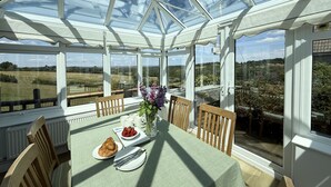 A conservatory with a table set for breakfast, featuring croissants, strawberries, and a vase with flowers. - Betty's Barn -  Evershot, Dorset (Evershot)