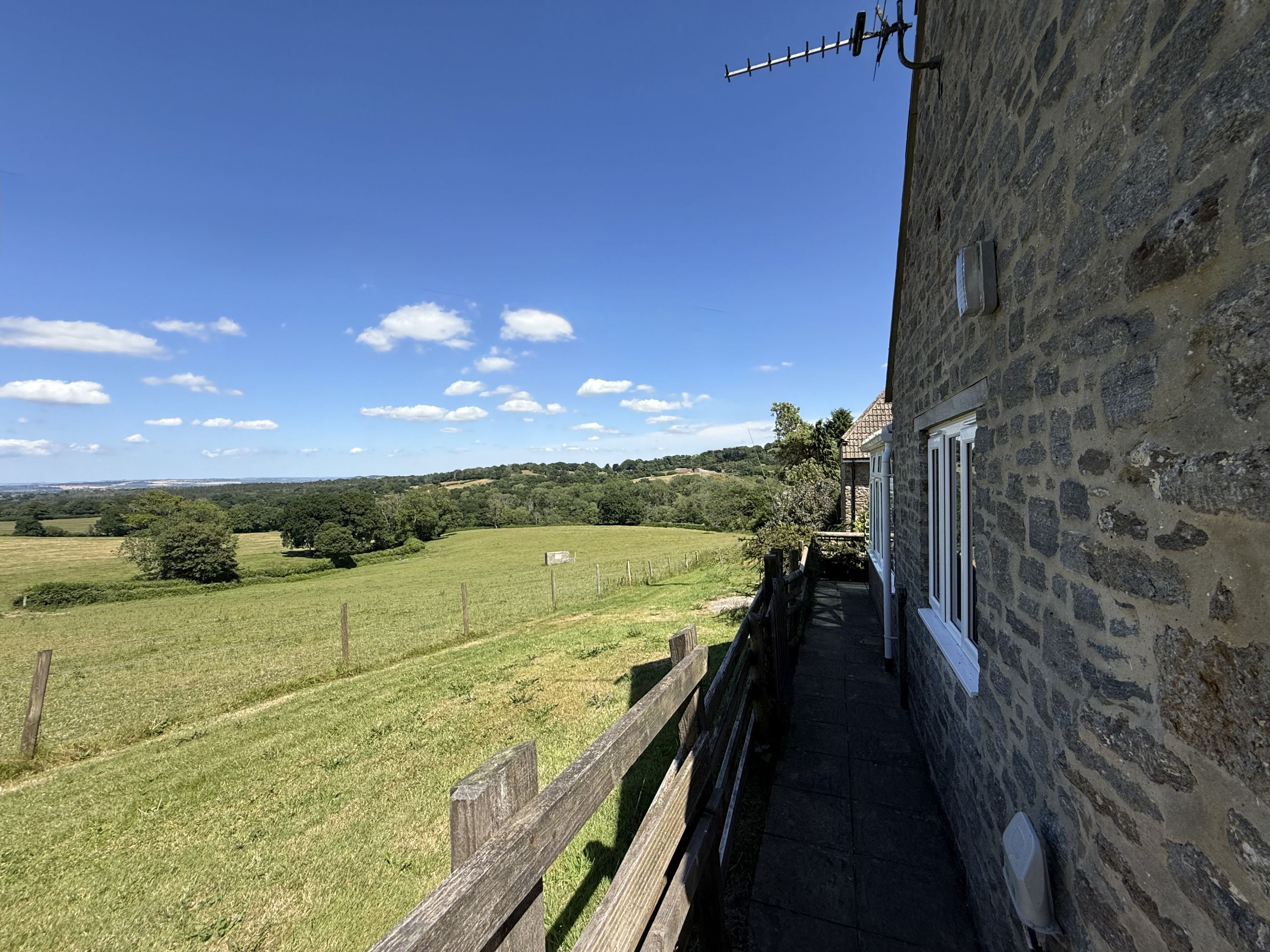 A stone building with a balcony overlooking a grassy field and a clear blue sky.