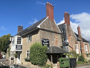 Ein historisches Gebäude mit einem Schild für Thomas Hardy's Historic Corn Inn, mit Steinmauern, Schornsteinen und einem großen grünen Busch.