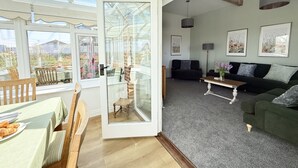A spacious living room with a large glass door leading to a conservatory, a green sofa, a coffee table, and framed artwork on the walls. - Betty's Barn -  Evershot, Dorset (Evershot)