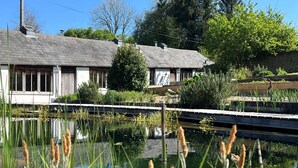 Ein Haus mit Teich im Vordergrund, umgeben von Grün und einer Holzterrasse.