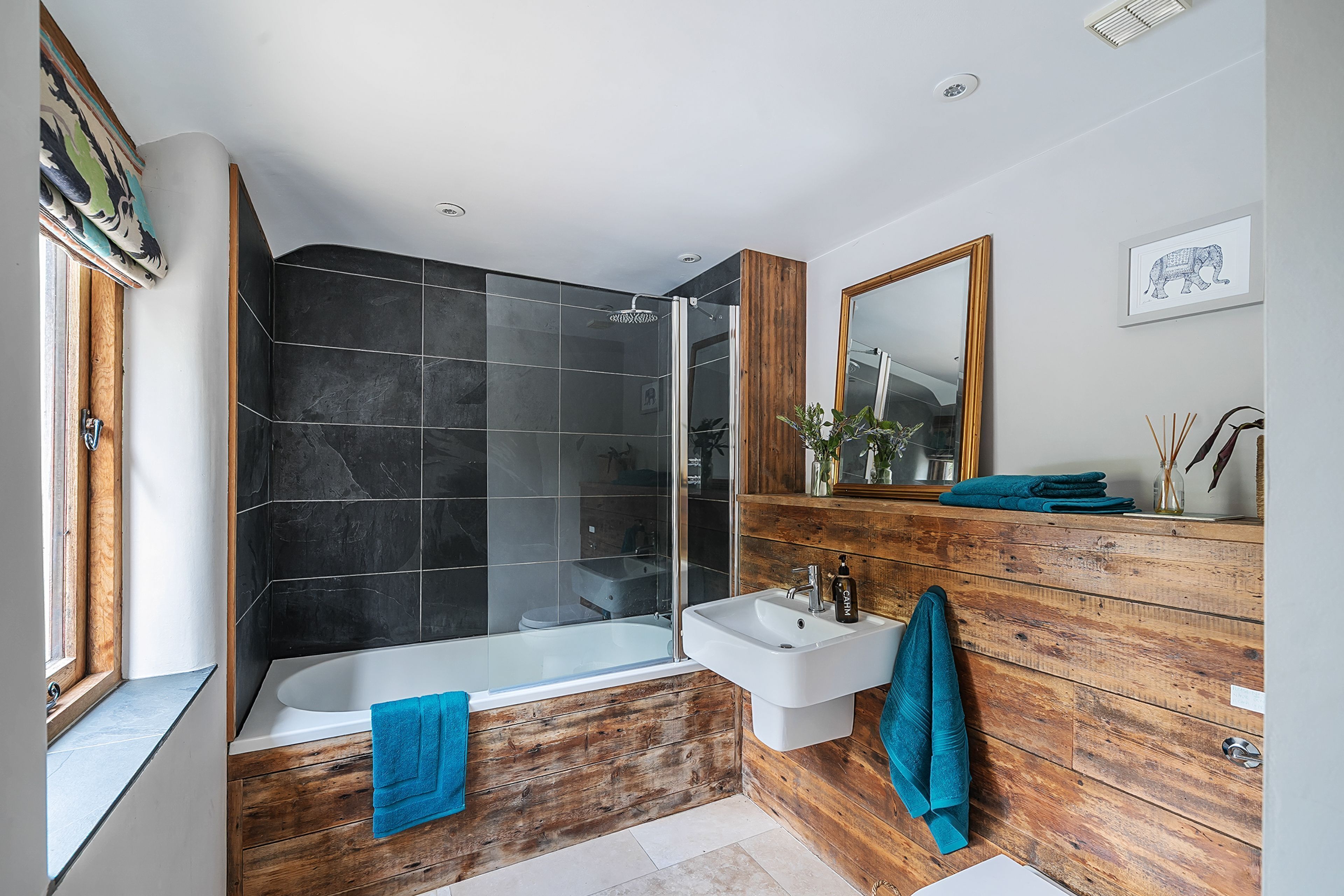 Ein modernes Badezimmer mit einer gläsernen Duschkabine, einer freistehenden Badewanne und einem Holz-Waschtisch.