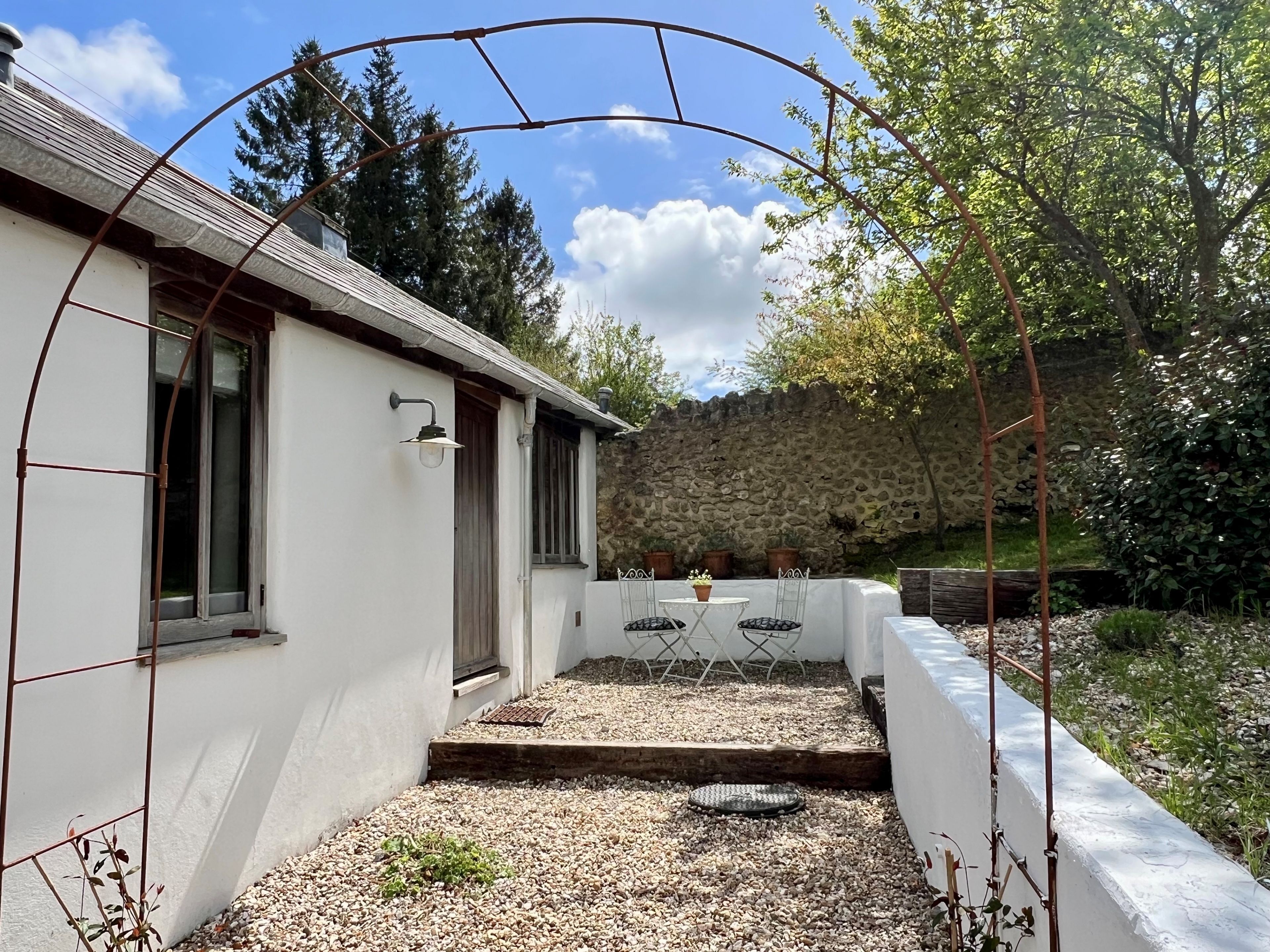 A white building with a stone wall and a garden area with a table and chairs.