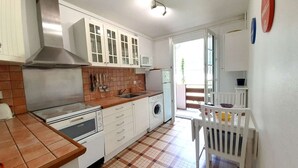 Een compacte keuken met witte kastjes, een roestvrijstalen afzuigkap, een magnetron en een wasmachine.