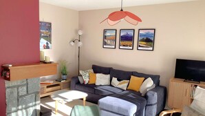 Een woonkamer met een bank, fauteuils, een televisie, een open haard en ingekaderde foto's aan de muur.