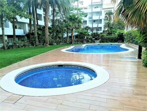 Two circular swimming pools with tiled edges, surrounded by a wooden deck and lush greenery. - Peaceful Apartment with Pool and Terrace in Roses (Roses)