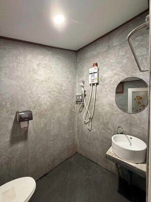 A bathroom with a marble wall, a toilet, a sink, a shower with a handheld showerhead, and a wall-mounted heater. - Baan Natee (Chiang Khan)