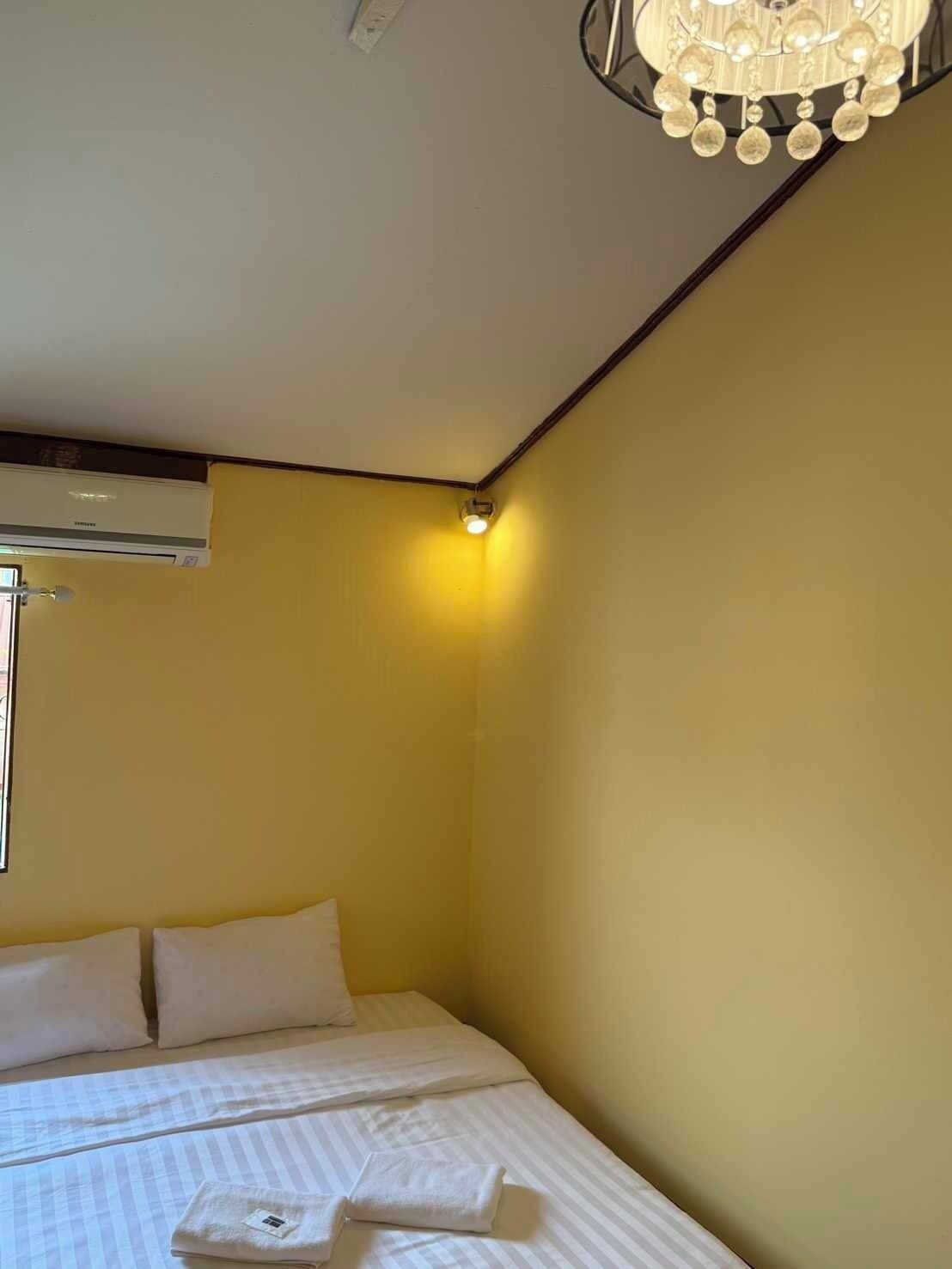 Una habitación de hotel con cama, almohadas, una lámpara en el techo y un equipo de aire acondicionado.
