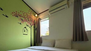 Ein Hotelzimmer mit Bett, Fenster mit Vorhängen, Klimaanlage und Wandbild von Vögeln und einem Baum.