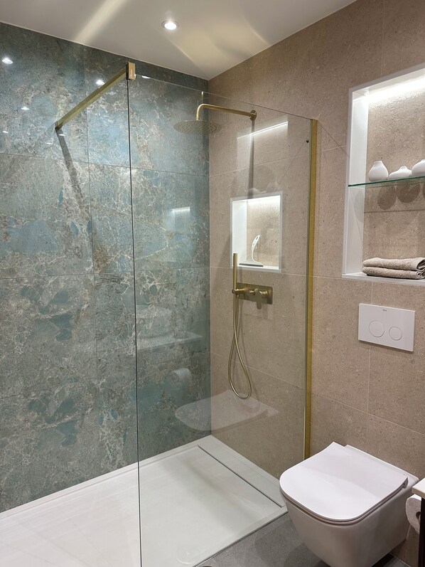 Un baño moderno con ducha de vidrio, inodoro y tocador con espejo y estantes.