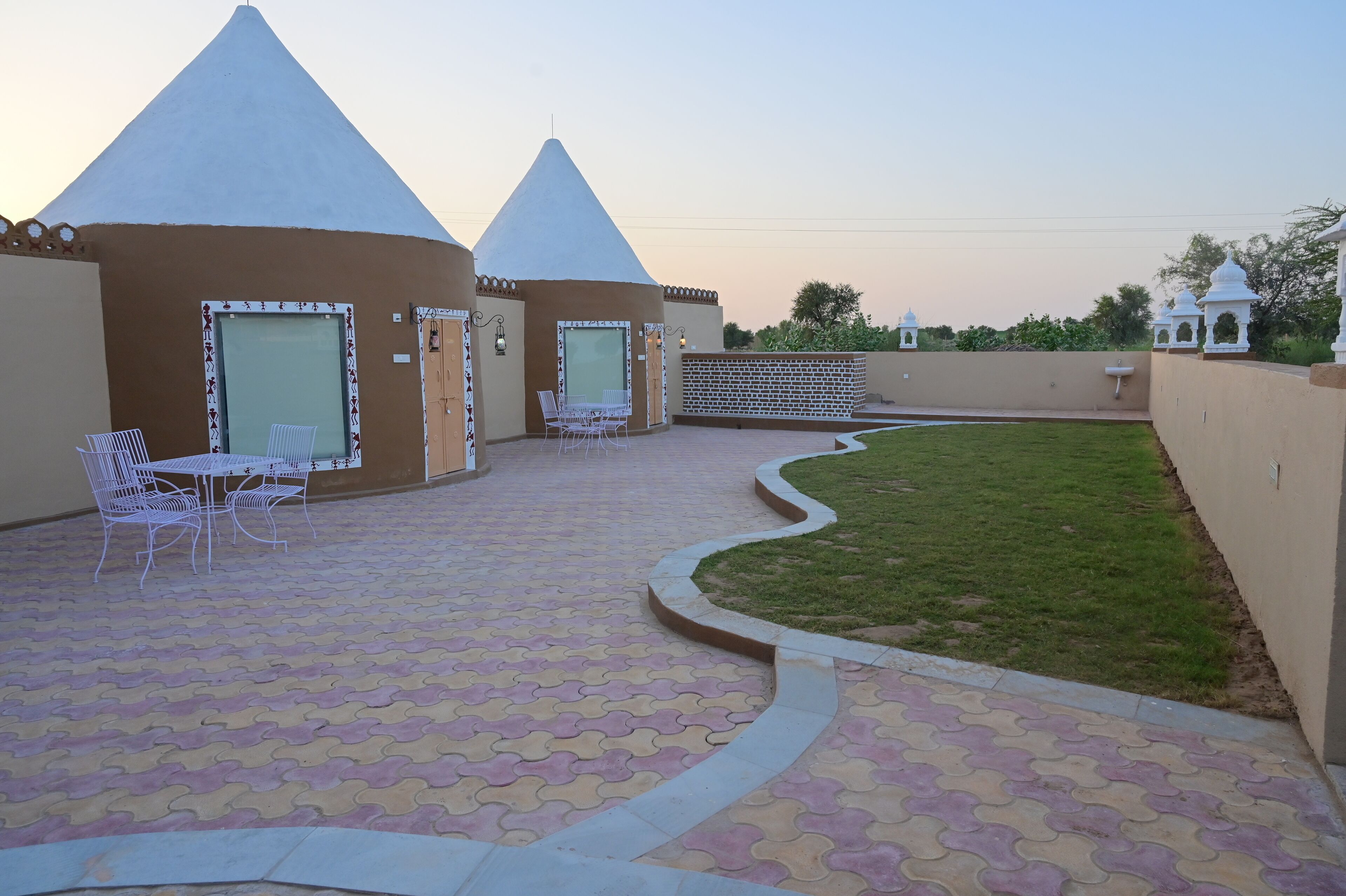A courtyard with two conical-roofed structures, a paved walkway, and a small lawn area.