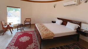Een slaapkamer met een bed, twee stoelen, een tafeltje, een raam en een airconditioning.