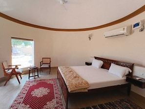Un dormitorio con una cama, dos sillas, una mesita, una ventana y un equipo de aire acondicionado.