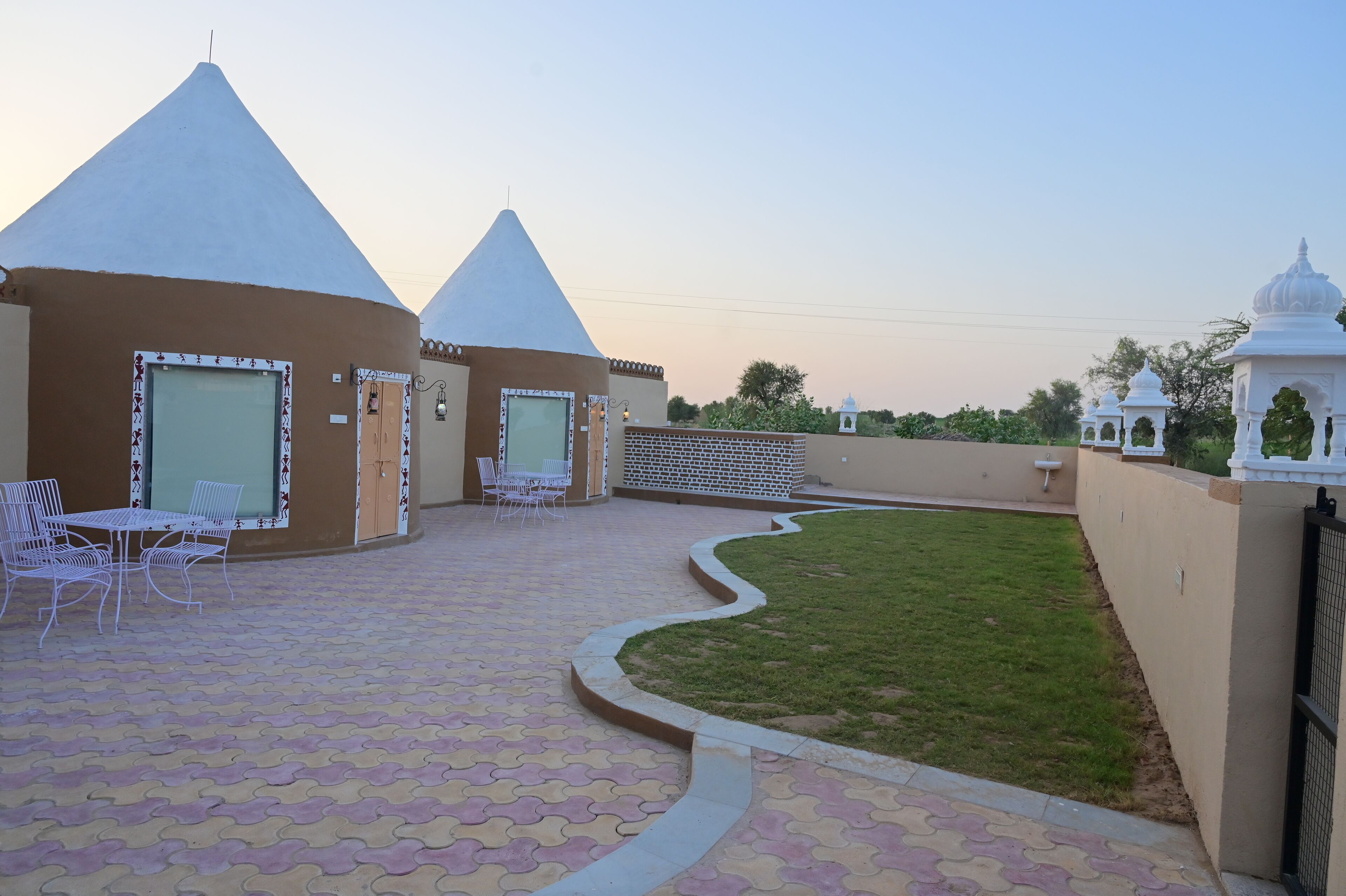 A courtyard with a tiled floor, a white outdoor seating area, and a white building with a conical roof.
