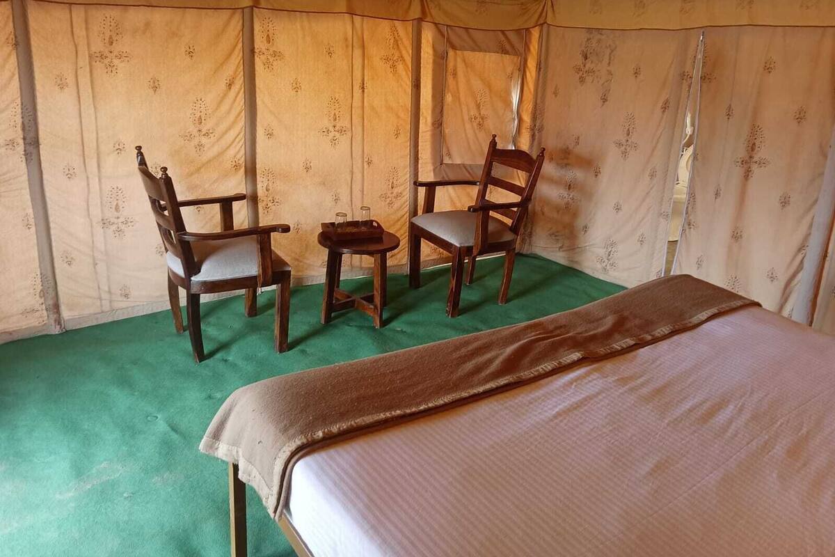 Una habitación con toldo, una cama, dos sillas de madera y una pequeña mesa.