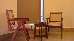 Een kamer met twee houten stoelen en een klein tafeltje, een verticale pilaar en een effen muur.