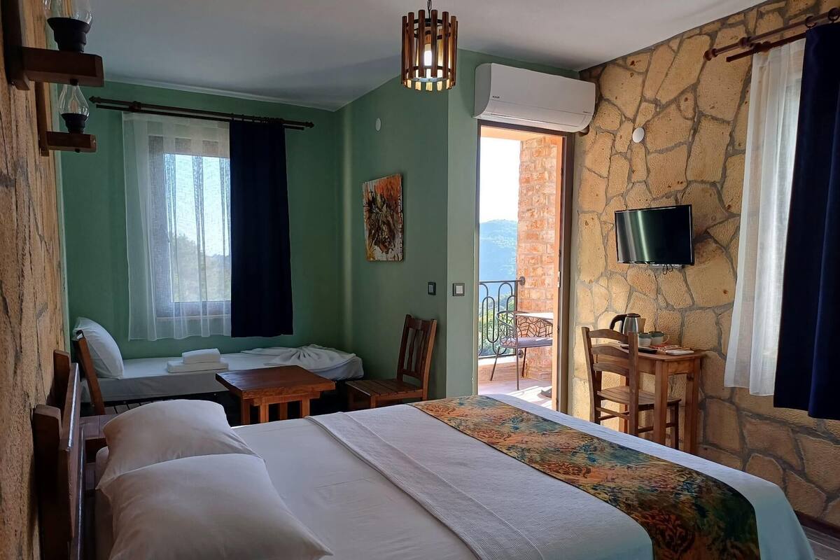 A hotel room with a bed, a desk, a chair, a TV, and a balcony with a view.