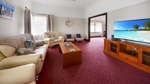 A living room with a beige sofa, two armchairs, a wooden coffee table, and a television on a wooden cabinet. - Beautifully restored 1930s gem, perfectly located in the heart of Portland. (Glenelg)