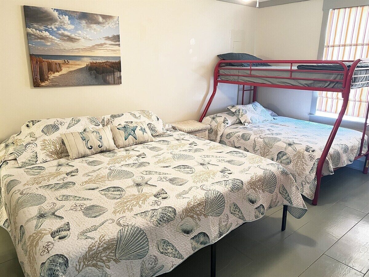 A room with two bunk beds, a beach-themed bedspread, and a painting of a beach scene.