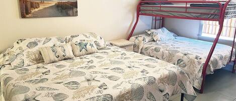 A room with two bunk beds, a beach-themed bedspread, and a painting of a beach scene.