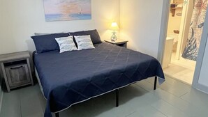 Un dormitorio con cama, mesita de noche, lámpara y un cuadro en la pared.