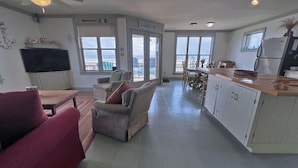 Un salón amplio con un sofá, un sillón pequeño, una mesa de comedor y una zona de cocina con armarios y una encimera.