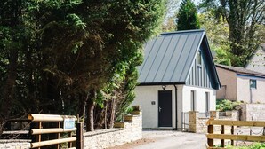A rustic lodge with a metal roof, a stone wall entrance, and a wooden gate. - Nice apartment for 2 guests with WIFI, TV and patio (Inverness)