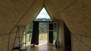 A triangular wooden room with a large window, a ladder, and a view of a green landscape. - OKON Highlands Cottages & Camp (Yenokavan)