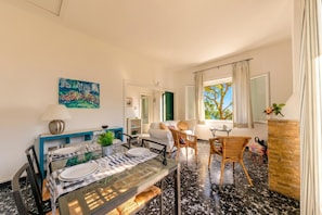 A dining area with a glass table, chairs, and a sofa in a bright room with a view. - Monterosso Apartments (Monterosso al Mare)