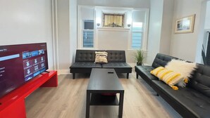 A modern living room with a flat-screen TV, two sofas, a coffee table, and a large window with blinds. - Spacious & Convenient near NYC (West New York)