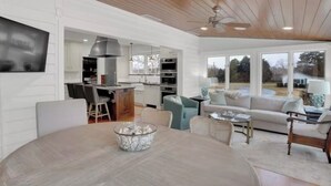 A modern kitchen with white cabinetry, a dining area with a round table, and a living room with a sofa and chairs.