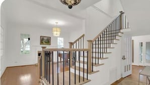 A spacious room with a wooden staircase, a chandelier, and a dining area.