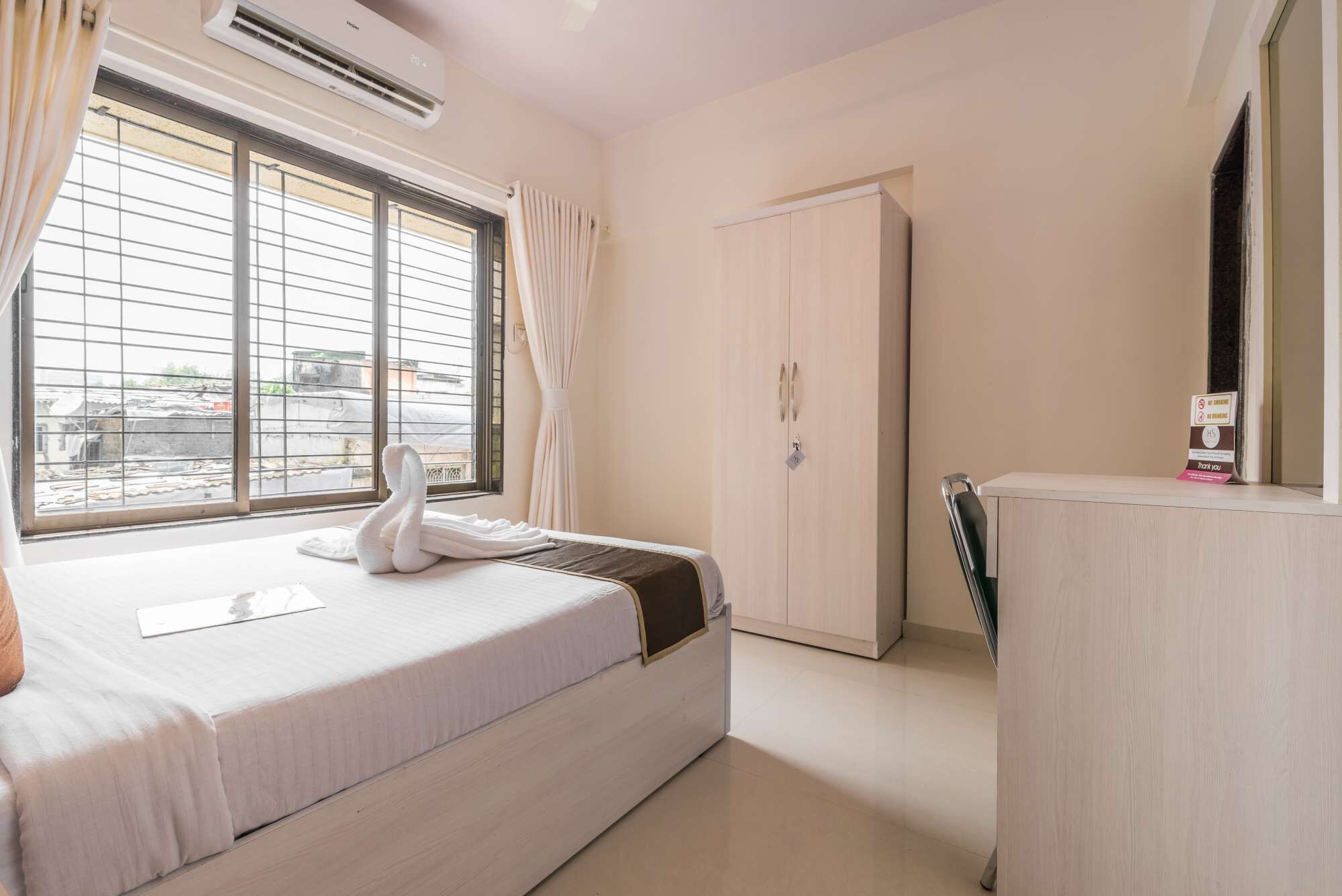 A hotel room with a bed, a wardrobe, a desk, and a window with curtains.