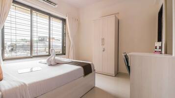 A hotel room with a bed, a wardrobe, a desk, and a window with curtains.