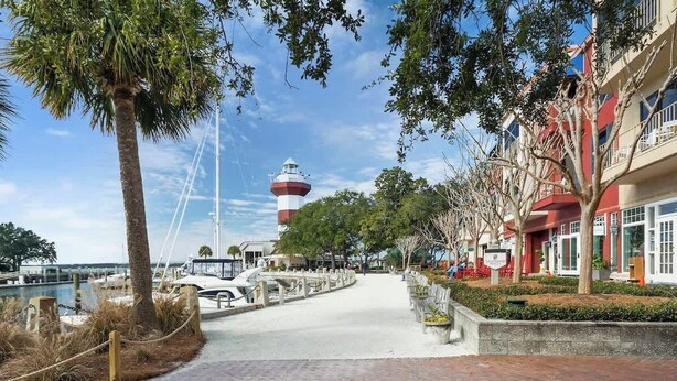 A waterfront promenade with a lighthouse, palm trees, and a marina. - 519 Plantation Club | Steps to Pool & Short Walk to Beach Access (Hilton Head Island)