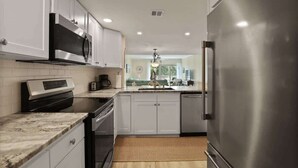 A modern kitchen with white cabinets, stainless steel appliances, and a wooden floor. - 519 Plantation Club | Steps to Pool & Short Walk to Beach Access (Hilton Head Island)