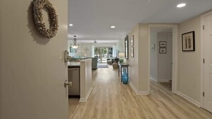 A hallway with a wooden floor, a door on the left, and a kitchen area in the background. - 519 Plantation Club | Steps to Pool & Short Walk to Beach Access (Hilton Head Island)