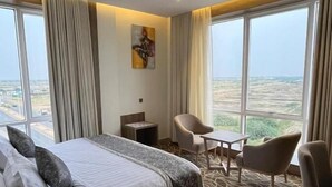 Ein Hotelzimmer mit einem großen Bett, einem Schreibtisch, zwei Stühlen und Blick auf die Landschaft durch große Fenster.