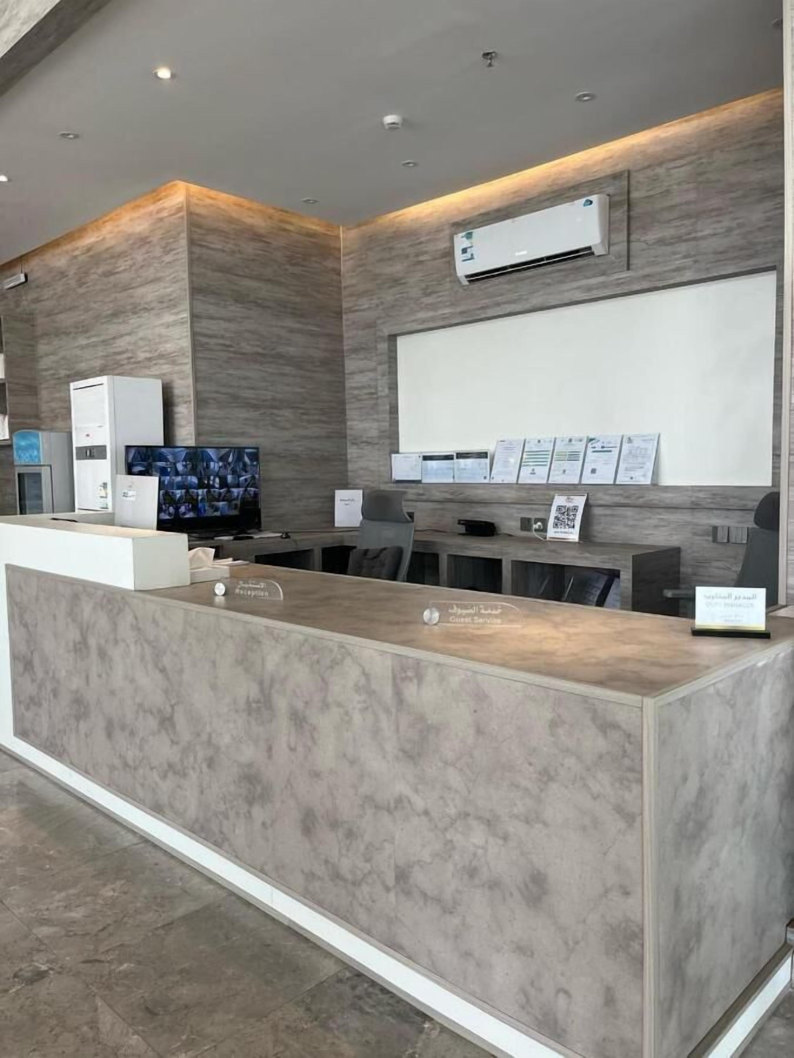 A reception desk with a marble finish, a mounted air conditioner, a flat-screen TV, and a wall-mounted information board.