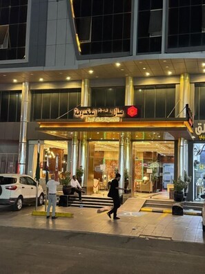 Entrada de hotel con diseño moderno, que destaca la puerta principal, un área de recepción y una escalera visible que conduce al interior.