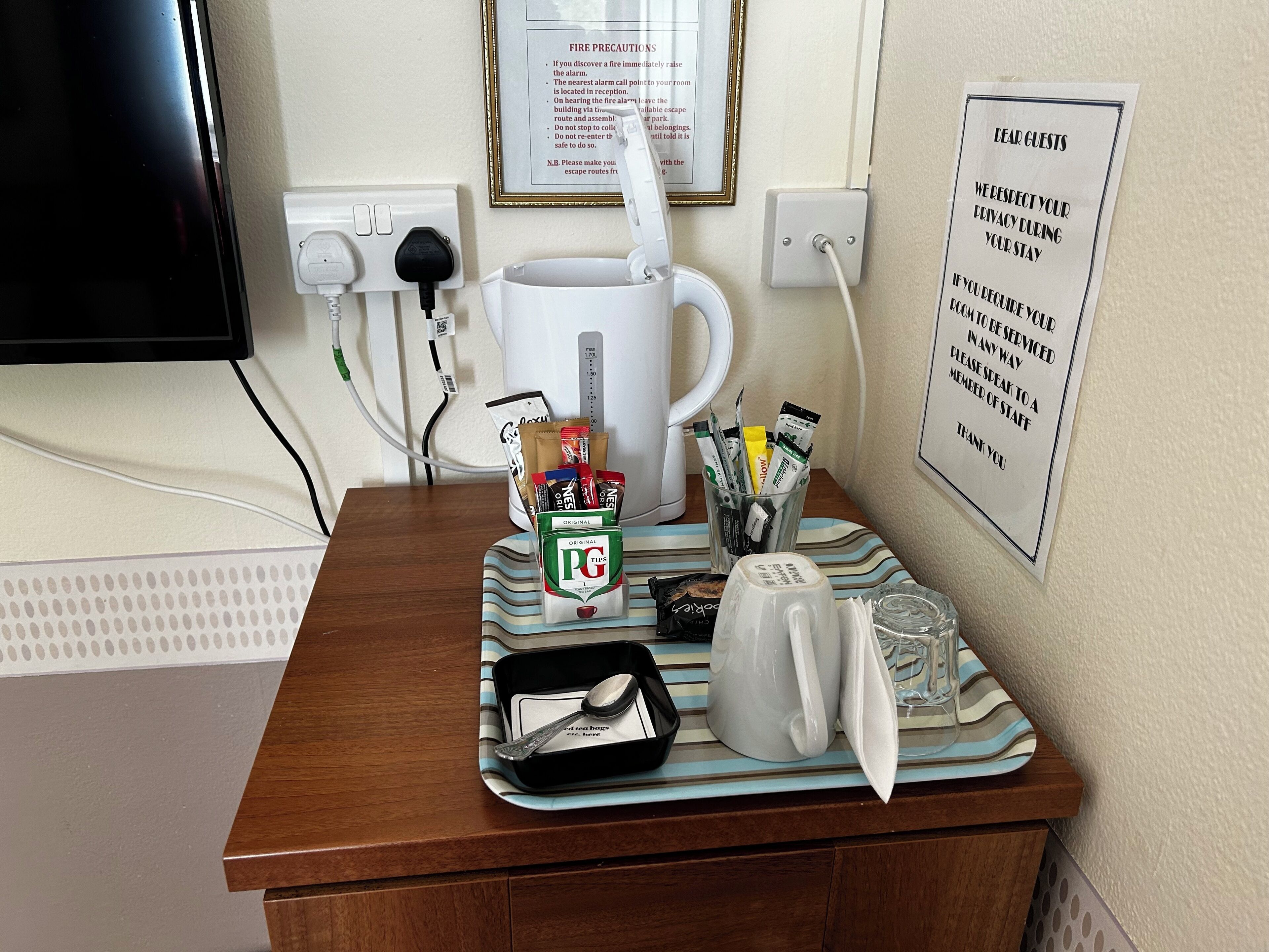 Une chambre d’hôtel équipée d’une machine à café, de sachets de thé, d’une tasse et d’une affiche encadrée sur les consignes de sécurité incendie, accrochée au mur.
