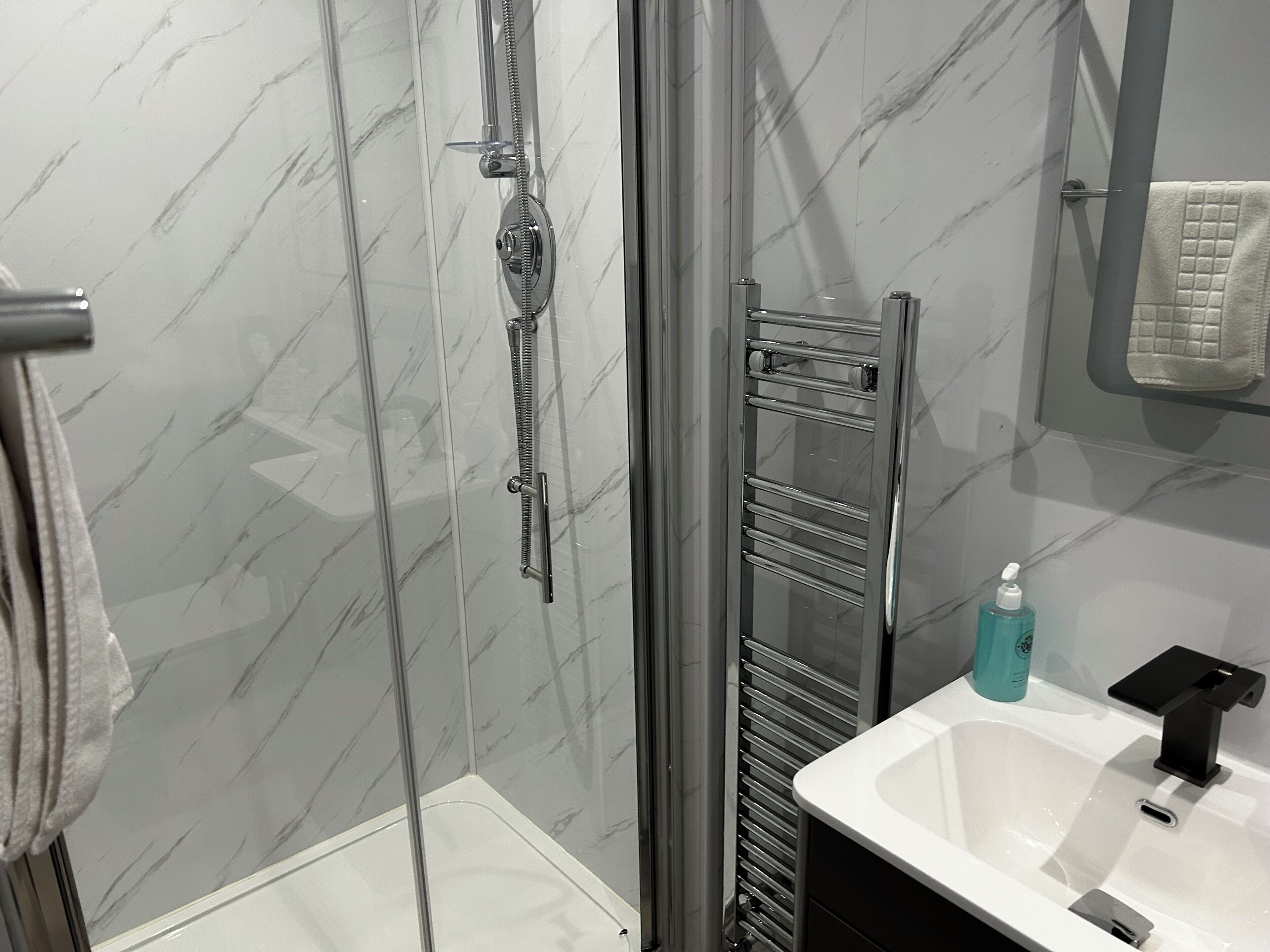 A bathroom with a glass-enclosed shower, a white sink, and a towel rack.