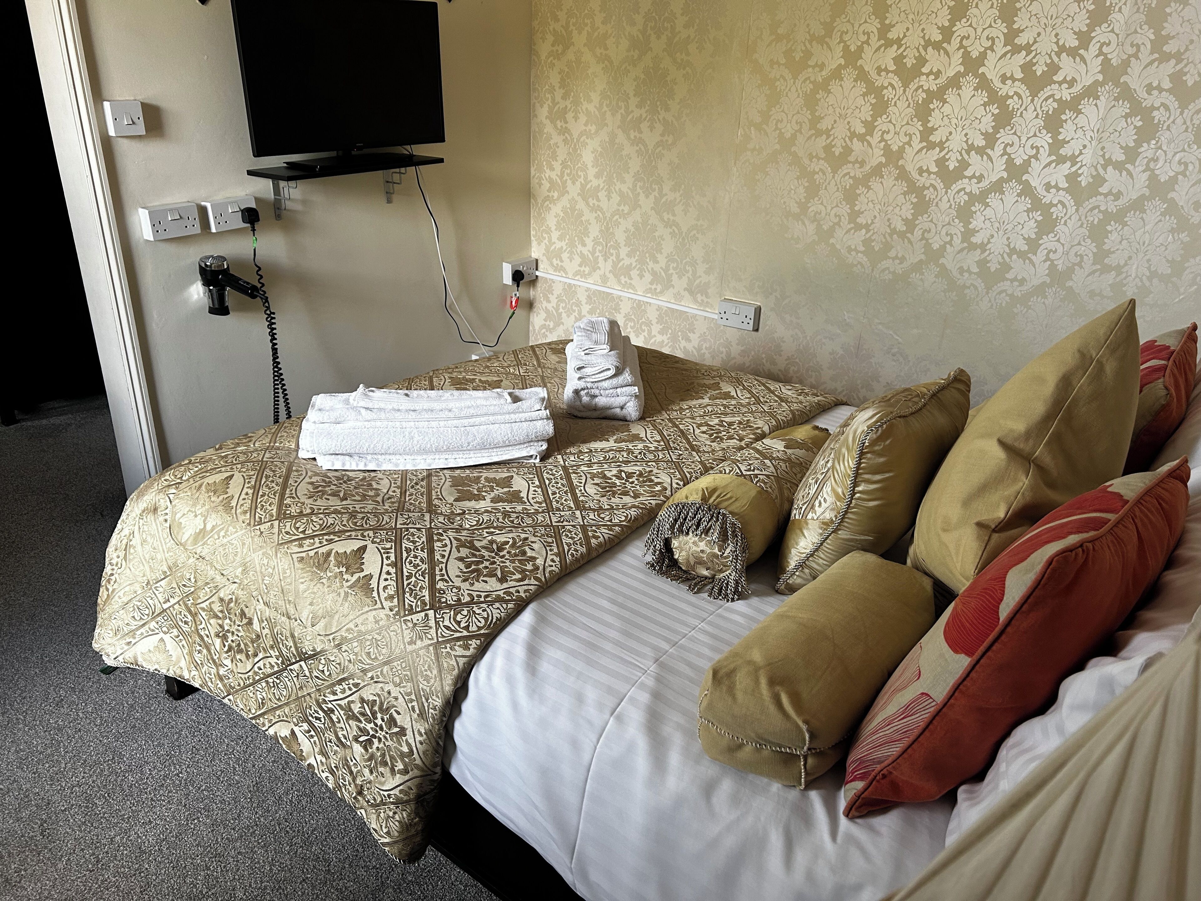A hotel room with a bed, pillows, a folded towel, a TV, and a telephone.