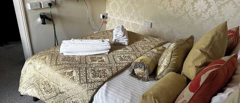 A hotel room with a bed, pillows, a folded towel, a TV, and a telephone.