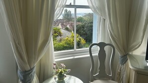 Ein Zimmer mit Fenster, Vorhängen, einem Stuhl und einem Tisch mit Blumenvase.