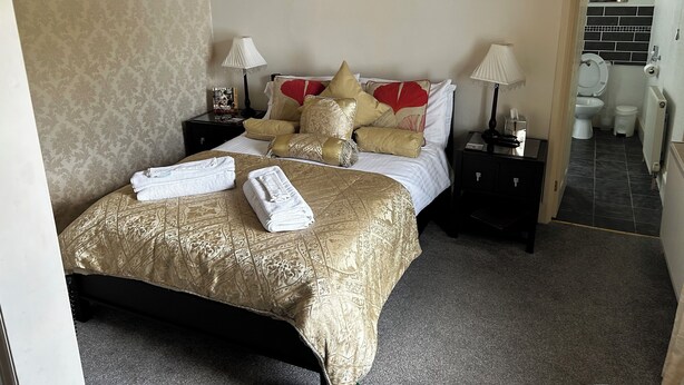 Ein Hotelzimmer mit einem Bett, zwei Nachttischen, einem Wandbild und einem durch eine offene Tür einsehbaren Badezimmer.