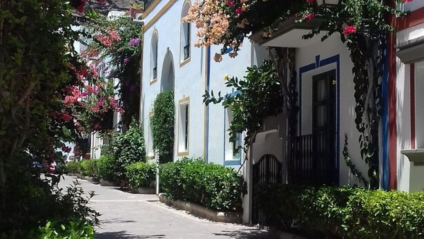 A narrow street with buildings on either side, some with balconies and flower boxes. - Mogan Playa 19 by El Sirocco (Lomo Quiebre)