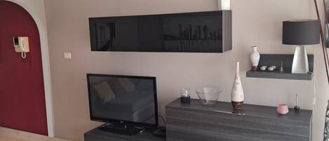 En moderne stue med et fladskærms-tv, møbler i mørkt træ, en rød farveaccent på væggen og en minimalistisk indretning.