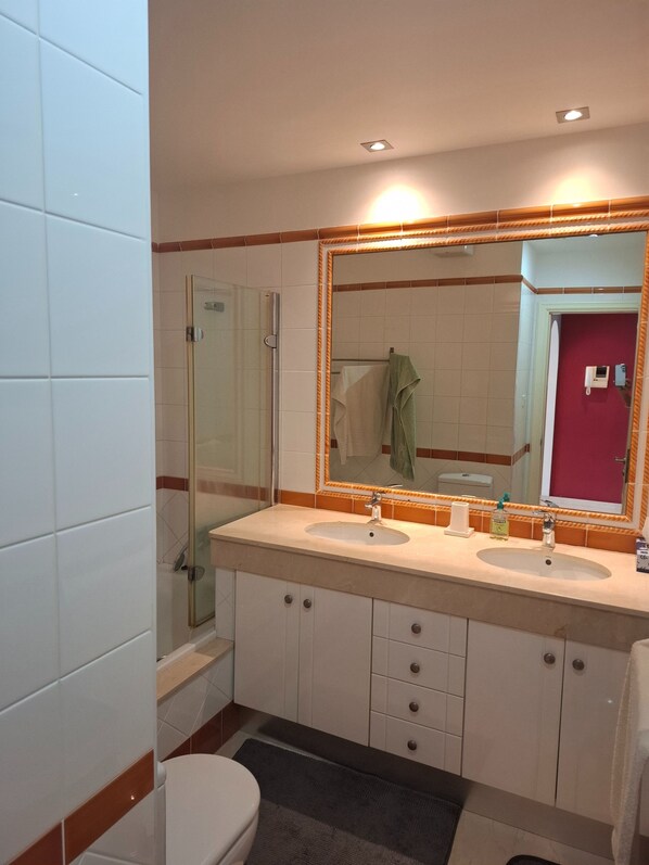 A bathroom with two sinks, a glass shower enclosure, a toilet, and a mirror with an orange frame.