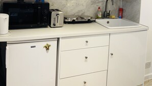 A modern kitchen with white cabinets, a microwave, a toaster, a sink, and a small refrigerator. - Brighton charm – Near Beach, City Centre & Station (Brighton and Hove)